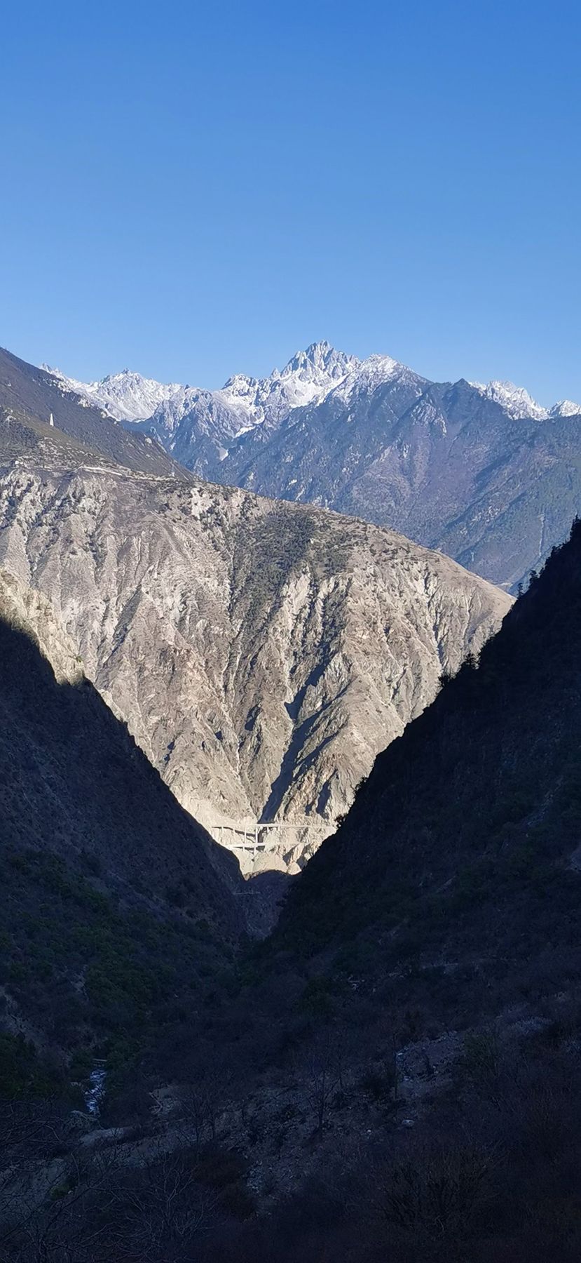 Un sommet enneigé au-dessus d’une vallée profonde en V, avec un pont routier en contrebas