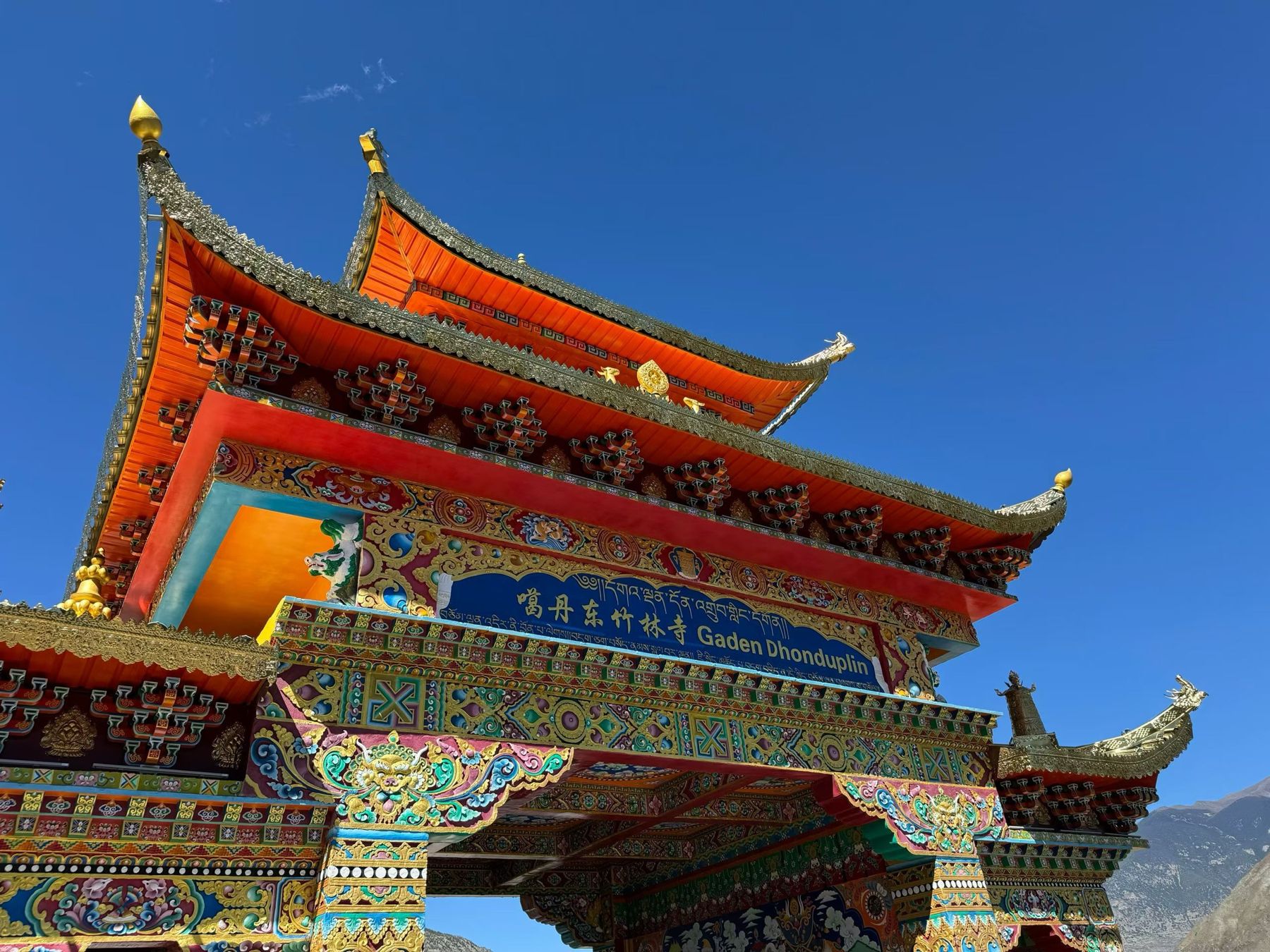 Le portail rouge et or richement peint d’un monastère tibétain sous un ciel bleu profond