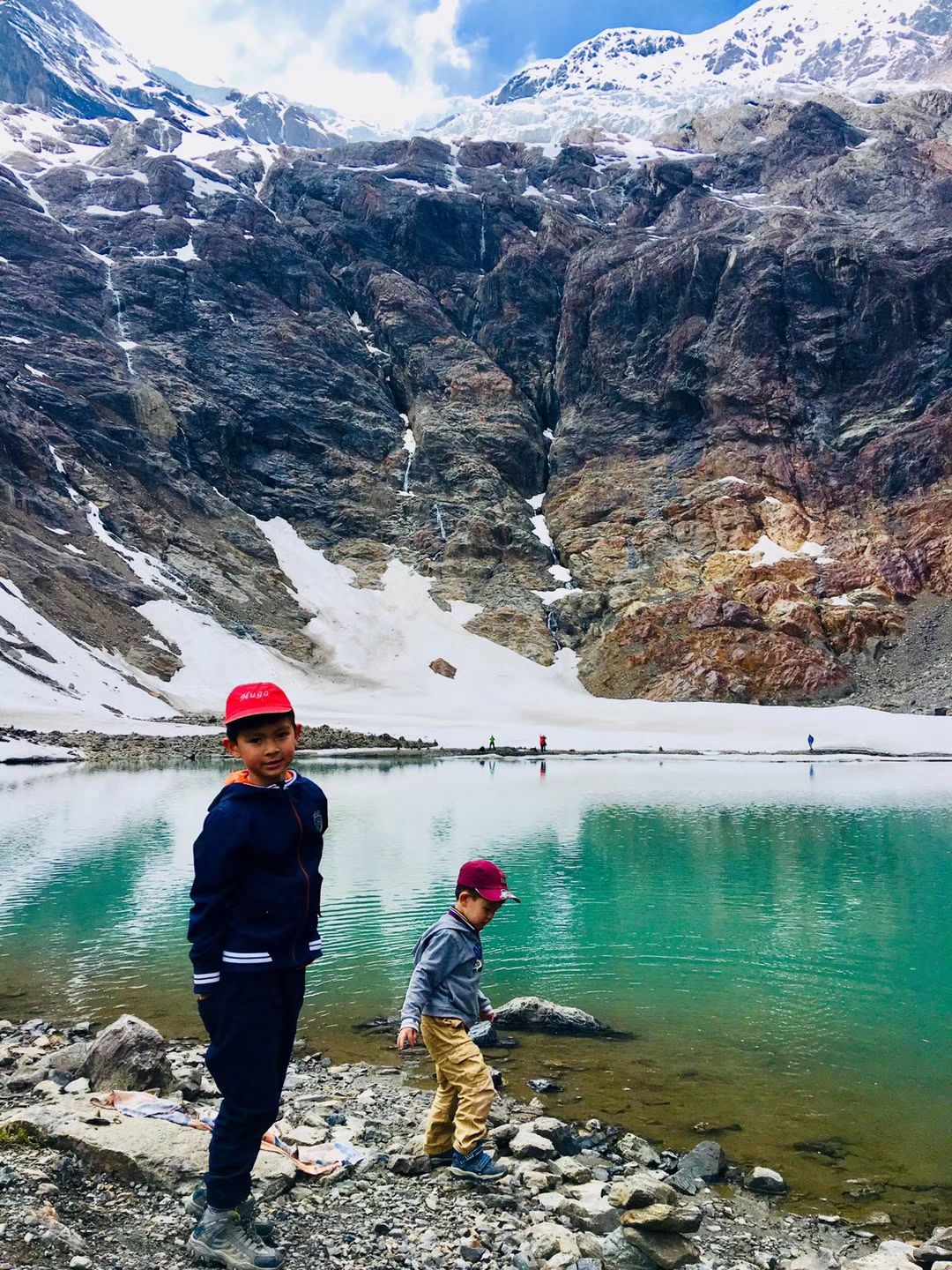 Deux garçons au bord d’un lac turquoise sous un cirque enneigé