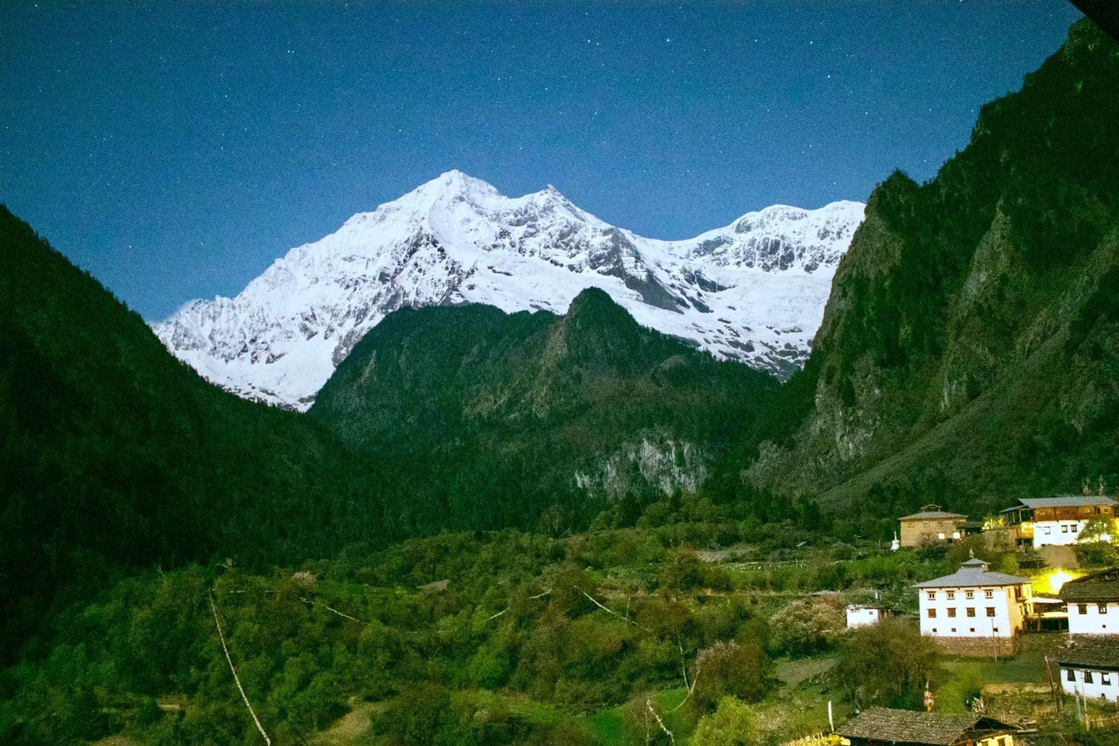 Un sommet enneigé sous un ciel étoilé au-dessus des maisons de Yubeng