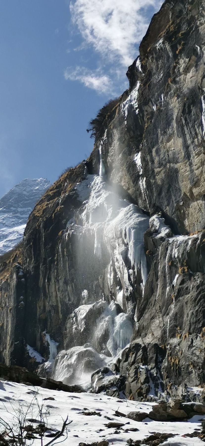 Une cascade gelée sur une paroi rocheuse, avec de la neige à son pied
