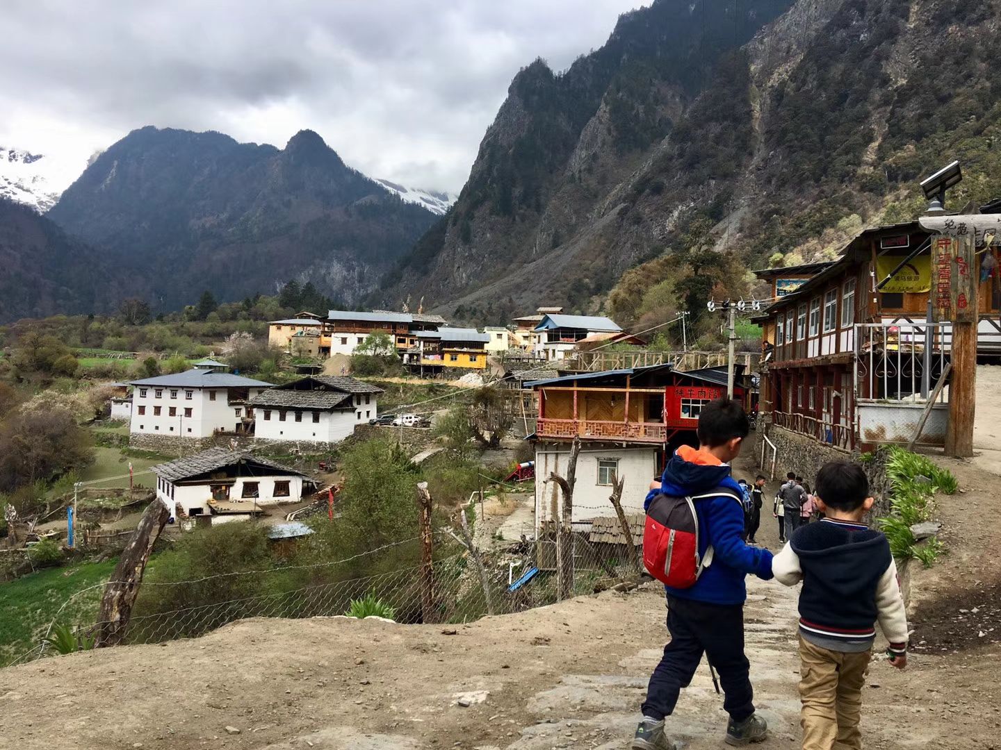 Deux enfants marchant vers les maisons de bois de Yubeng haut, sous une montagne