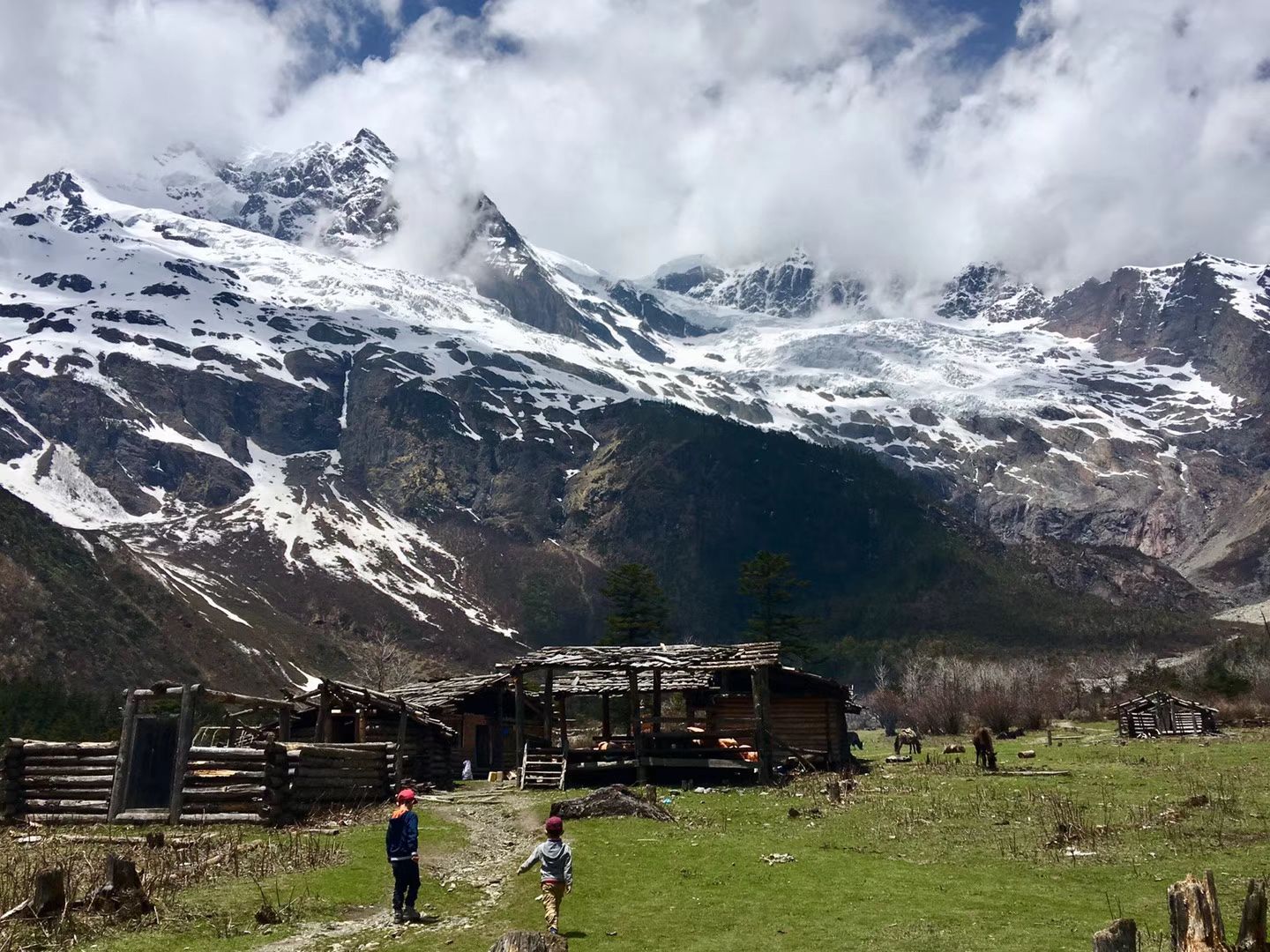 Des cabanes en bois dans un alpage vert sous des sommets glaciaires