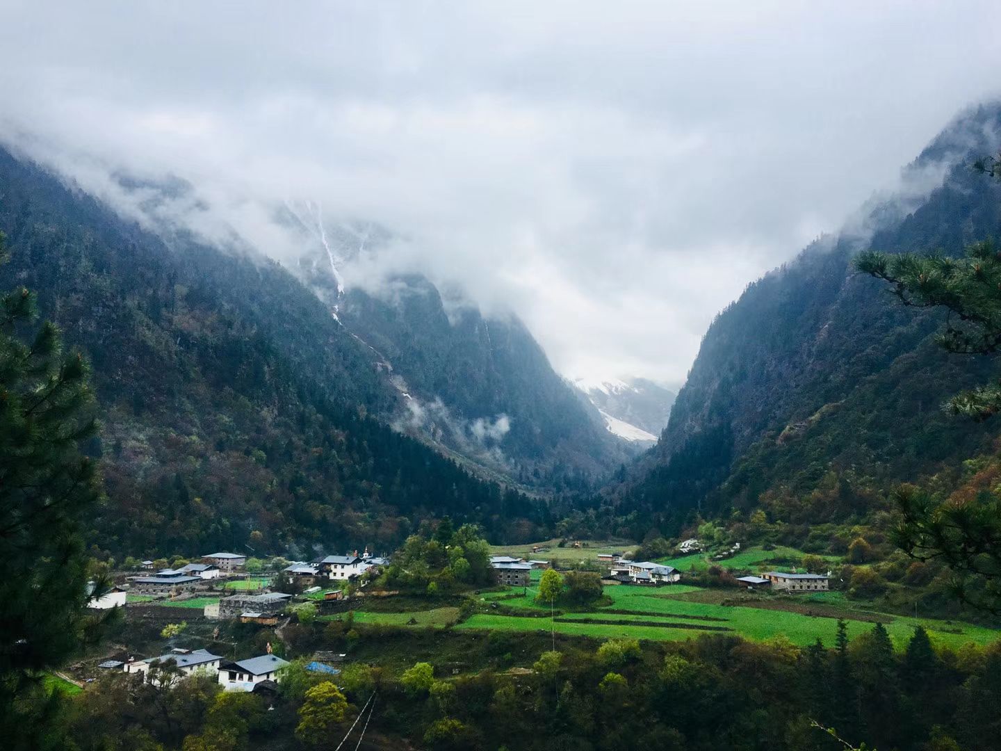 Un village au milieu de champs verts dans une vallée sous des nuages bas